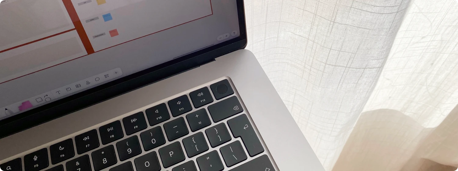 Close-up of a laptop with a presentation slide on the screen. Soft natural light is filtering through a curtain.